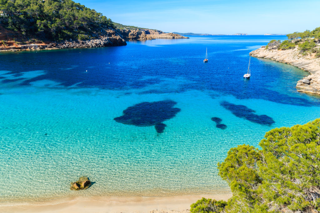 An aerial view of the Cala Salada bay in Ibiza, Spain with clear water, boats and greenery on the coast