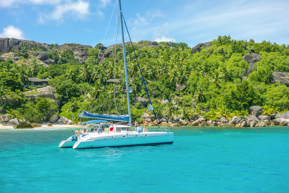 A catamaran in a bay in the Seychelles, little Island with palm trees with granite rocks in the ocean
