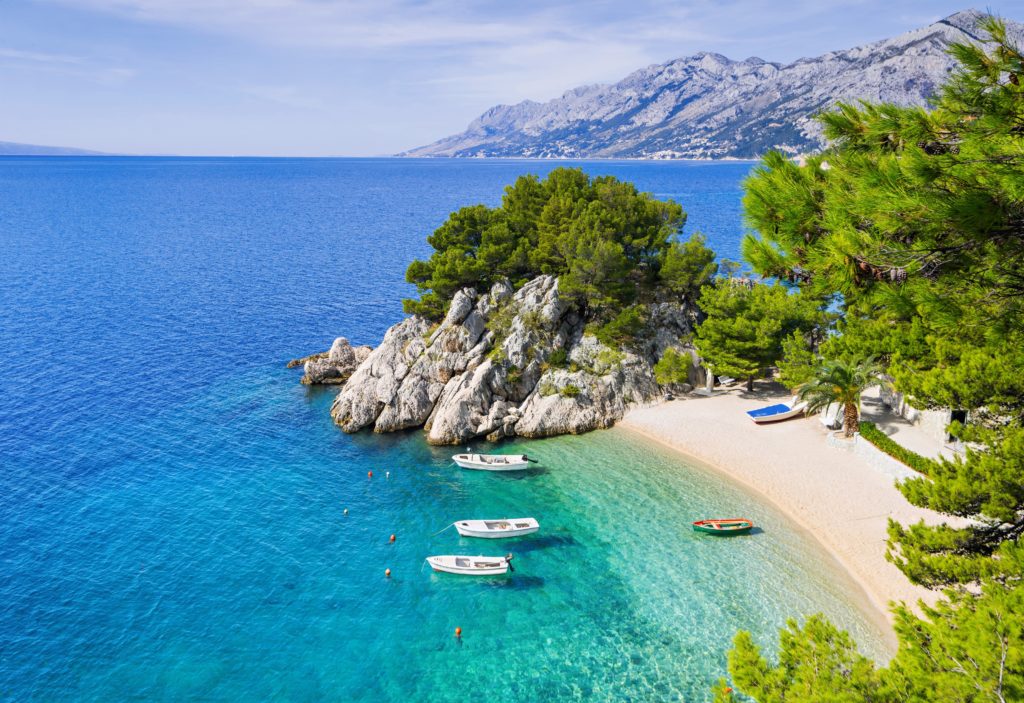 Aerial view of a bay with clear water, white sand, cliffs, surrounding greenery and a few boats 