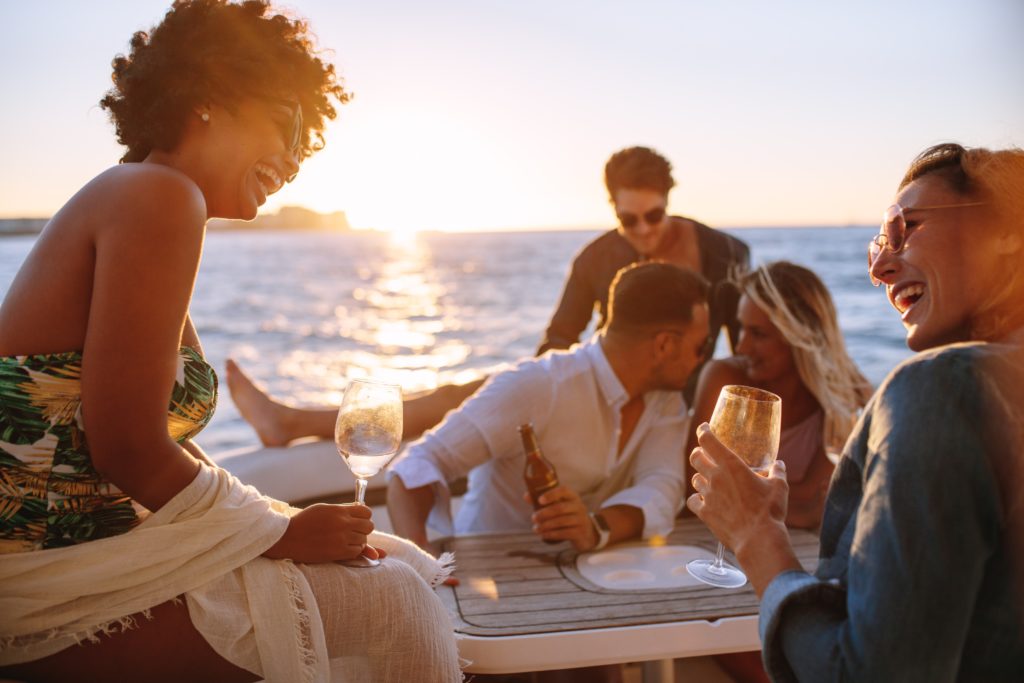 View of a group of friends on the boat in the sunset drinking and laughing 