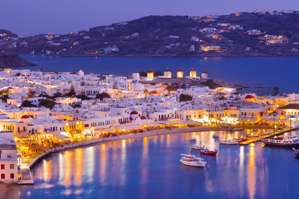 An evening aerial view of the bay of Mykonos with white washed buildings along the coast