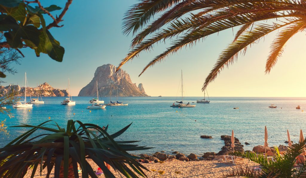 view of a sandy beach in Ibiza with sailboats in the background