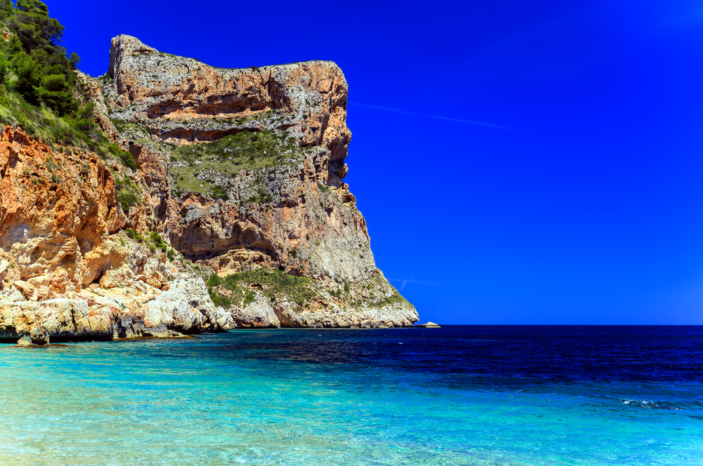 View of the Cala Dels Testos in the Alicante region of Spain, showing the blue sea and the imposant cliffs