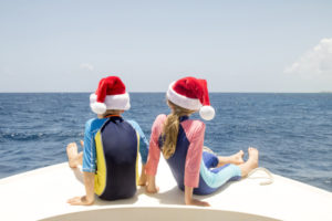 Siblings sitting in the front of boat with christmas hats on